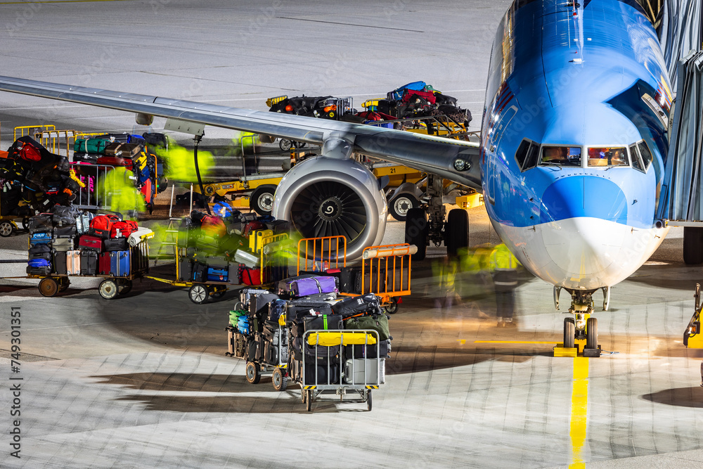 Fototapeta premium Baggage ground handling on the airport ramp. Workers loading a passenger airlplane with lots of baggage and cargo.