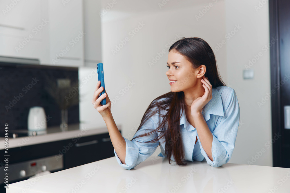 A woman sitting at a kitchen counter, holding phone up to ear, looking at screen, browsing or making a call A woman sitting at a kitchen counter, holding phone up to ear, looking at screen, browsing or making a call