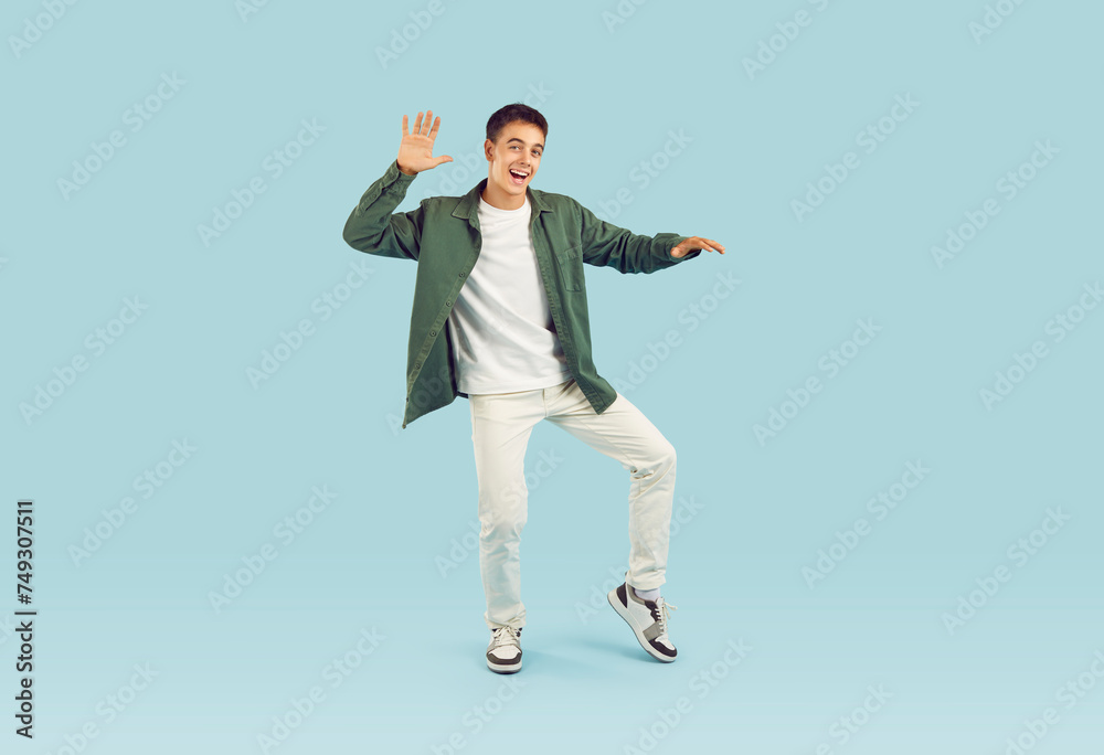 Full body portrait of a happy, cheerful, smiling young man or teenage boy in casual clothes dancing isolated on a light blue color background. Party, music, fun concept Full body portrait of a happy, cheerful, smiling young man or teenage boy in casual clothes dancing isolated on a light blue color background. Party, music, fun concept