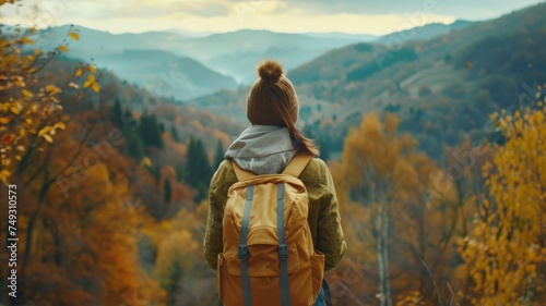 A beautiful woman with a backpack stands with her back turned and looking into the distance at the mountains. Inspiring travel lifestyle Autumn landscape.