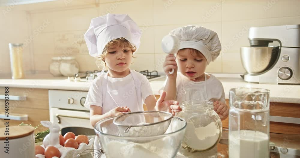 Two toddlers in chef hats cooking and sharing recipes in a kitchen Two toddlers in chef hats cooking and sharing recipes in a kitchen