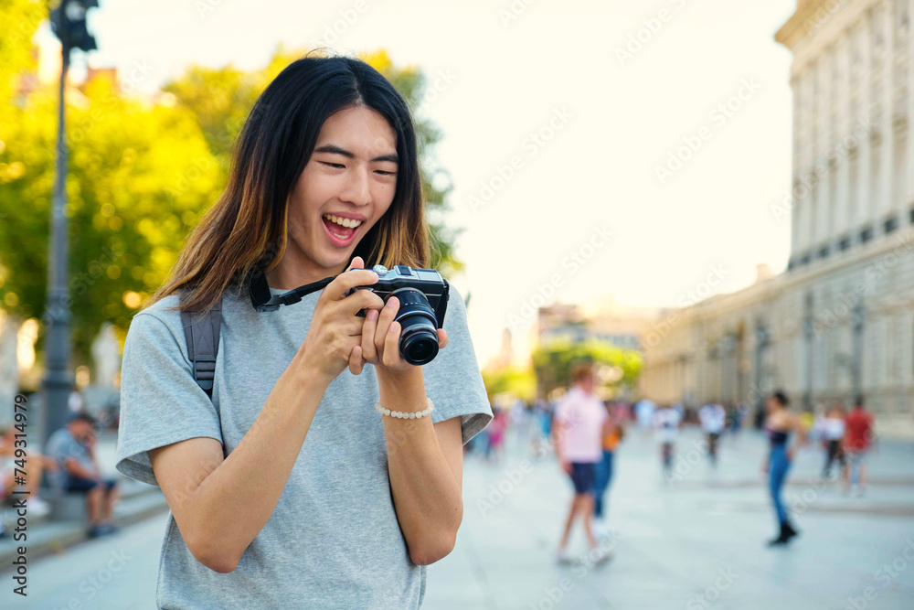 Taiwanese male tourist smiling and looking at photos in his camera while sightseeing in Madrid, Spain.