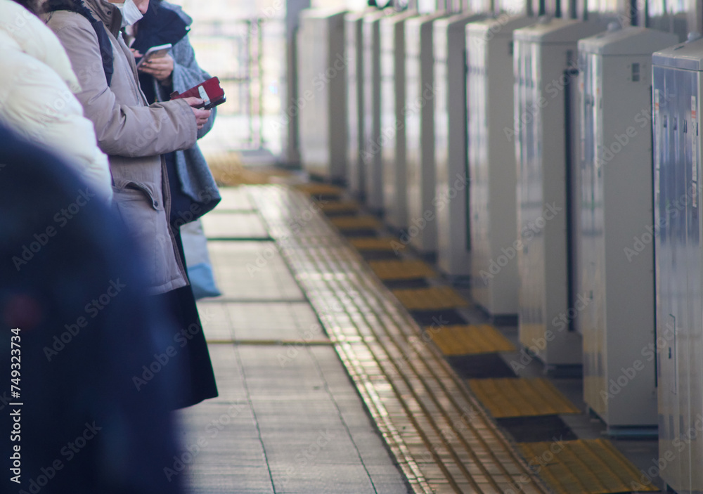 冬の朝の通勤時間の名古屋駅のホームで携帯電話を見ながら電車待ちの人々
