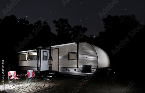 Forest silhouetted by stars with camping trailer