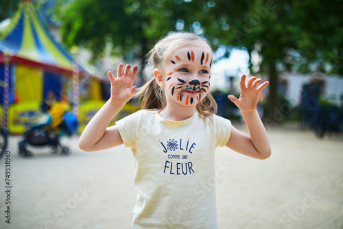 Little preschooler girl with tiger face painting outdoors photo