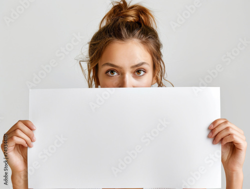 Woman with Half-Face Behind Blank Sign.
Young woman's face partially hidden behind a blank white sign, invoking curiosity. photo