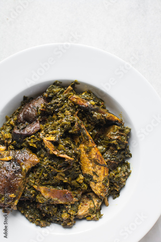 Nigerian vegetable soup with fish and bush meat in a white plate, afang soup in a large dinner plate, traditional edikang ikong soup in a white dish photo