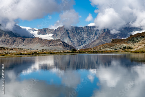 Panoramic view over the water of the Riffelsee near Zermatt, Switzerland towards Monte Rosa massif in eastern part of the Pennine Alps just north of the Matterhorn with mountains reflected in water