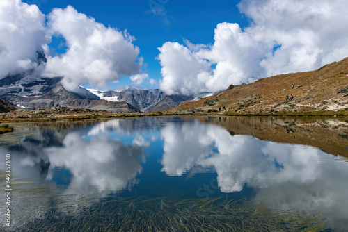 Panoramic view over the water of the Riffelsee near Zermatt, Switzerland towards Monte Rosa massif in eastern part of the Pennine Alps just north of the Matterhorn with mountains reflected in water