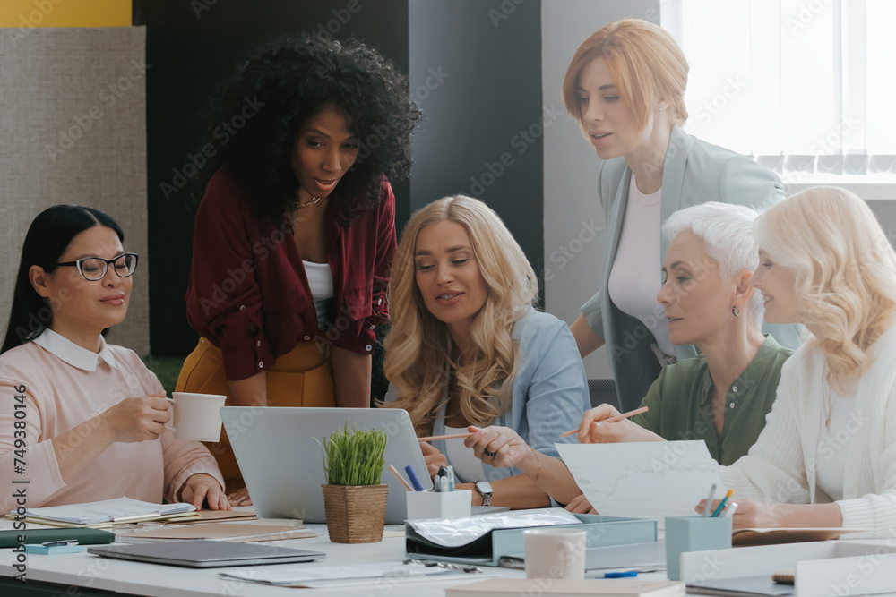 Obraz premium Group of mature women using laptop while discussing business in the office together
