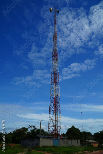 Red and white cell phone mast, radio communication station against bright blue sky. Itacoatiara, Amazonas state, Brazil.