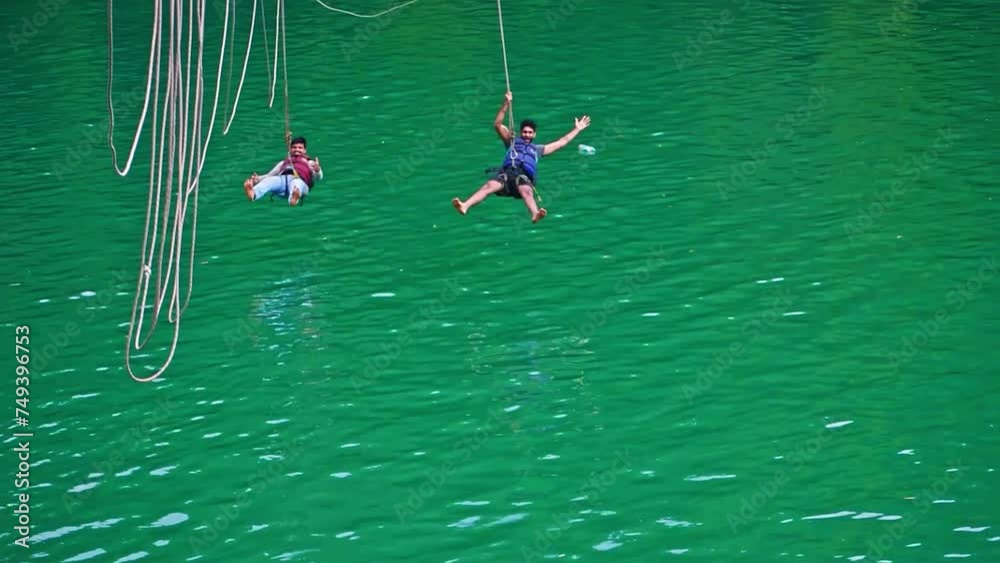 Two young tourist having fun at zipline, sliding over the river, slow motion footage.