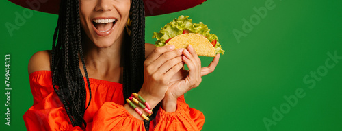 Close-up of happy young Mexican woman in Sombrero holding taco against green background