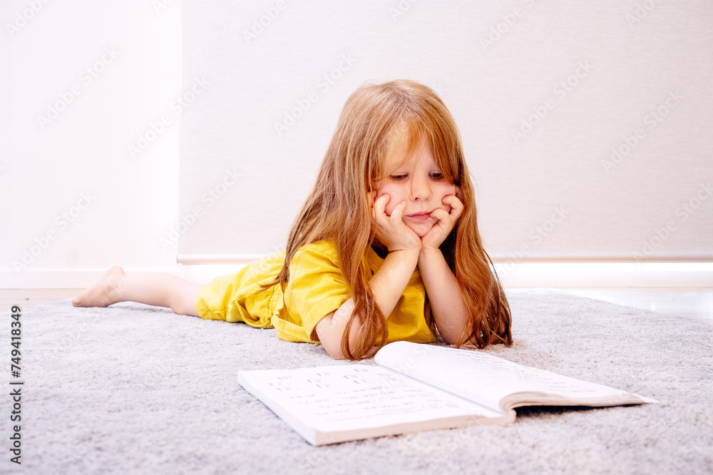 little girl lies on the carpet and reads a book little girl lies on the carpet and reads a book