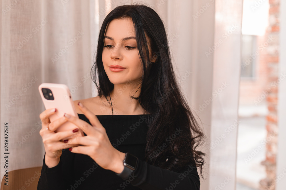 Portrait of calm teen female dressed casually holding mobile phone, typing messages, communicating with friends via social networks, using high Internet connection at cafe. Woman look flirting.