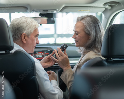 Mature Caucasian couple sitting in a new car and rejoicing at the purchase. 