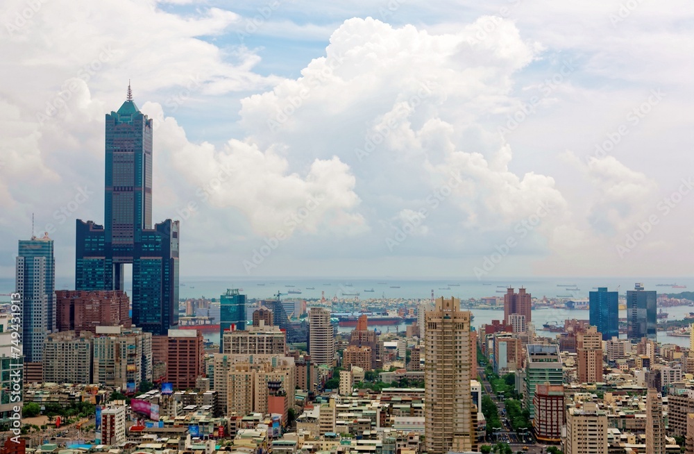 Cityscape of Kaohsiung Downtown, a vibrant seaport city in Southern Taiwan, with the landmark 85 Sky Tower standing out among modern buildings and ships parking in the harbor under cloudy sunny sky