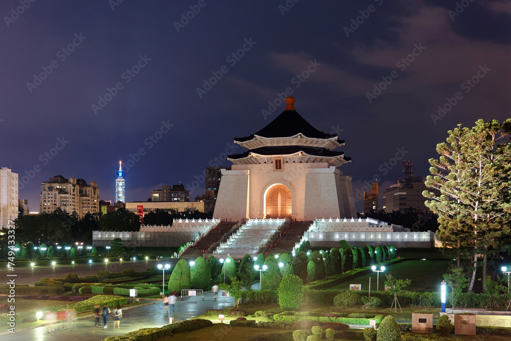 Naklejka premium Night scenery of Chiang Kai-Shek Memorial Hall by Liberty Square, a landmark and tourist attraction in Taipei, Taiwan, with the famous 101 Tower standing among high-rise buildings in the background