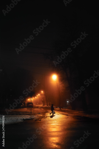 Street in fog with lanterns along road with man crossing the street, vertical photo