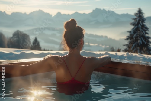 a young beautiful woman on ski vacation relaxing with her back turned in a warm soapy bathtub looking at the snowy mountains enjoying the view