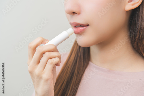 Lip care protection concept  pretty asian young woman  girl hand applying lipstick balm with moisturising on dry mouth from natural beauty product  skincare routine  makeup and cosmetics on background