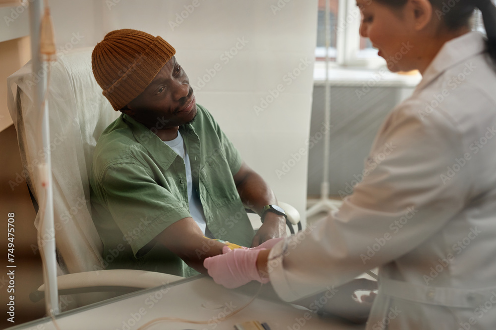 Portrait of African American man receiving chemotherapy treatment in procedure room at clinic behind glass copy space