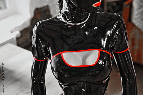 Dekolletee - Latex Fetisch Model / Latex Domina mit schwarzem Hochglanz Latex Outfit / Catsuit, eng geschnürtem, schwarzem Latex Korsett, Edelstahl Halsreif und großen Silikonbrüsten 