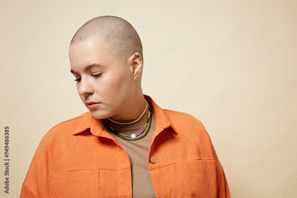 Obraz premium Minimal portrait of bald young woman wearing bright orange jacket looking away in studio, copy space