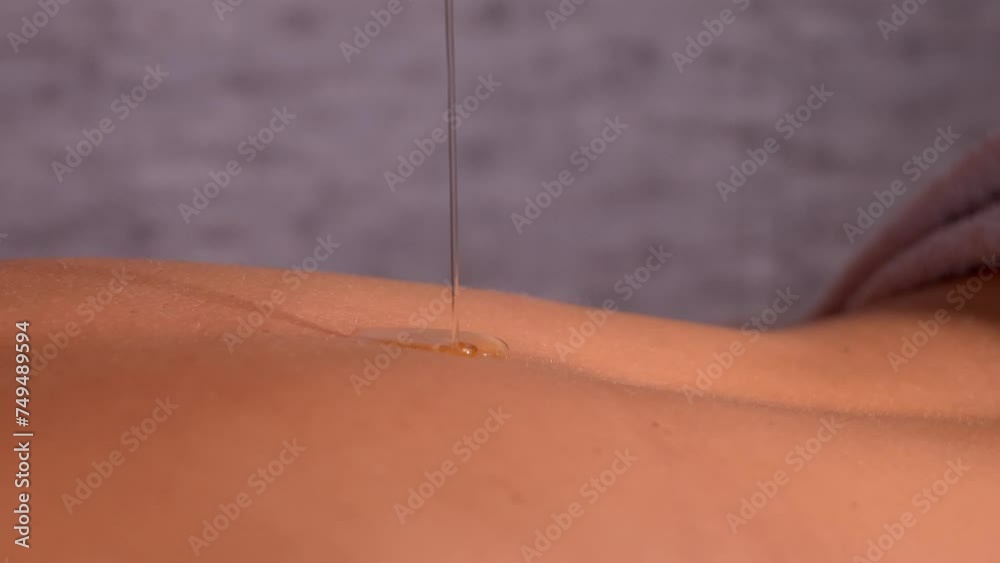 Close-up of jet aromatic oil in slow motion dousing back of woman. Masseuse getting ready to do oriental spa treatment for relaxing treatment. Therapist doing aromatherapy oil massage on female body. Close-up of jet aromatic oil in slow motion dousing back of woman. Masseuse getting ready to do oriental spa treatment for relaxing treatment. Therapist doing aromatherapy oil massage on female body.