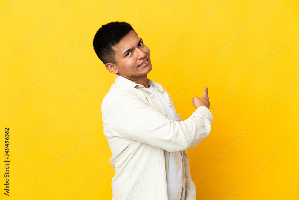 Young Ecuadorian man isolated on yellow background pointing back