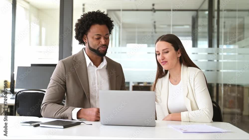 A professional meeting between a man and a woman, both dressed in business attire, discussing documents over a laptop in a bright office setting. A professional meeting between a man and a woman, both dressed in business attire, discussing documents over a laptop in a bright office setting.