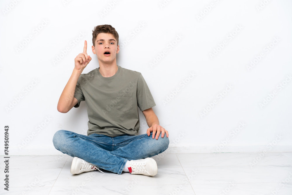 Teenager Russian man sitting on the floor isolated on white background thinking an idea pointing the finger up