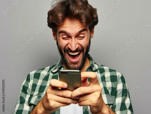 Portrait of a young man laughing while using mobile phone against grey background. Online Casino and Betting Concept with Copy Space. Gambling Concept.