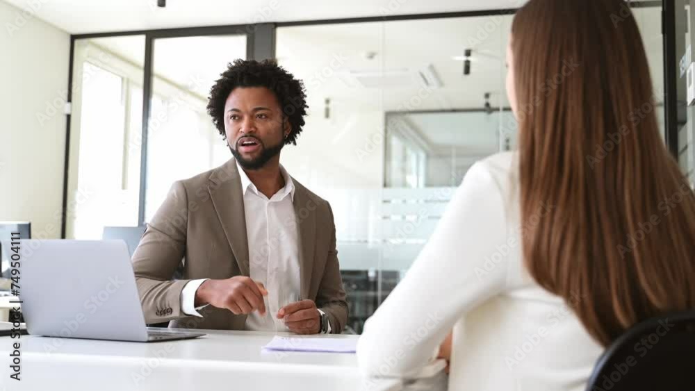 A focused businessman in a modern beige suit articulates a point during an engaging office discussion with a female colleague, whose presence is implied by her over-the-shoulder perspective A focused businessman in a modern beige suit articulates a point during an engaging office discussion with a female colleague, whose presence is implied by her over-the-shoulder perspective