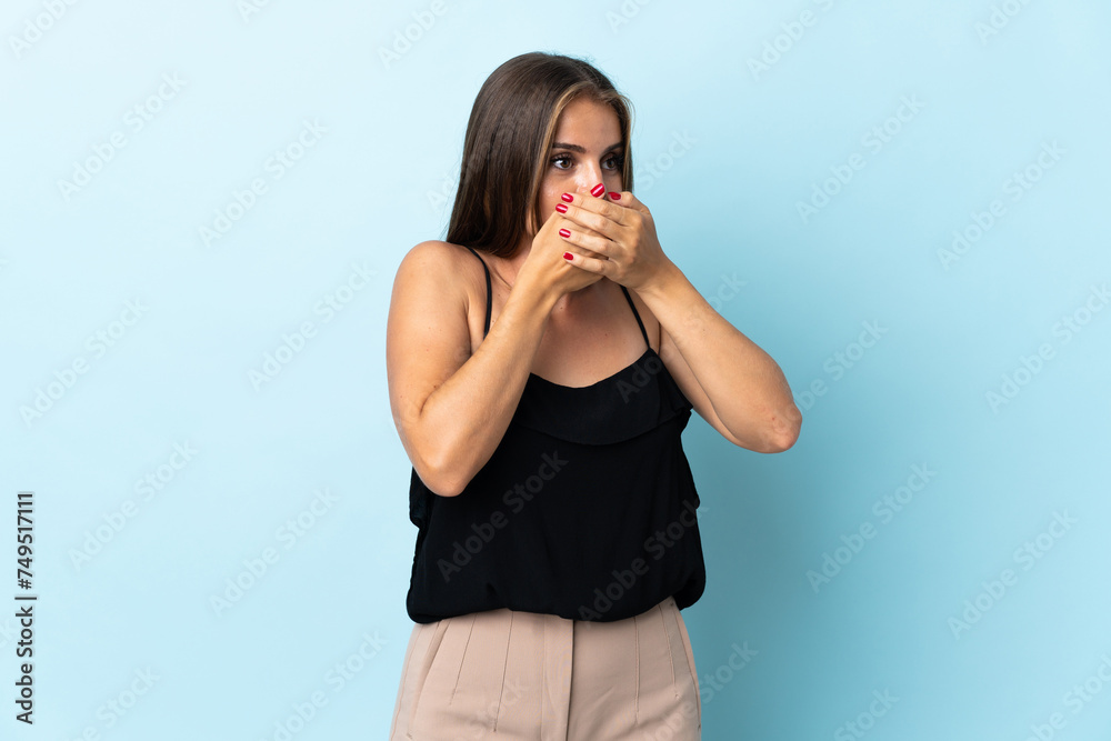 Young Uruguayan woman isolated on blue background covering mouth and looking to the side Young Uruguayan woman isolated on blue background covering mouth and looking to the side
