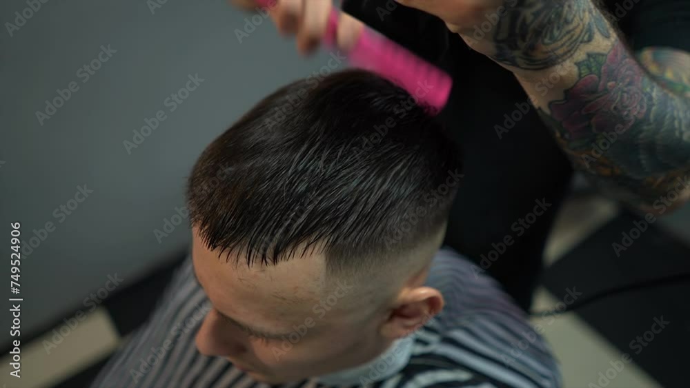 A barber man with a tattoo on his arm makes a haircut to a brunette guy in a barbershop, cuts his hair with a clipper close-up A barber man with a tattoo on his arm makes a haircut to a brunette guy in a barbershop, cuts his hair with a clipper close-up