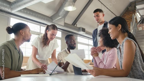 Smiling multi-cultural business team meeting around table in modern open plan office discussing document and collaborating together - shot in slow motion