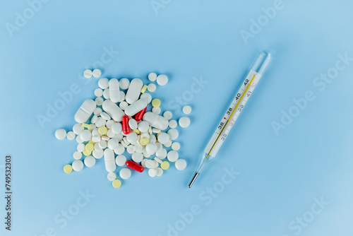 a scattering of different pills on a blue background and a thermometer with a temperature of 37 degrees photo