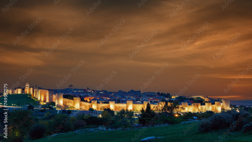 Panoramic view of the city of Avila, with its famous illuminated medieval walls surrounding the city at dusk