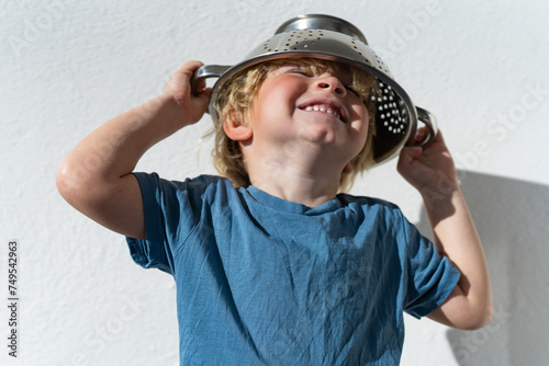 Little boy putting colander on his head . cheerful blond boy with a sieve on his head. positive kid