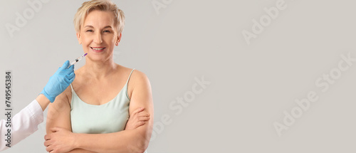 Mature woman receiving filler injection on grey background with space for text