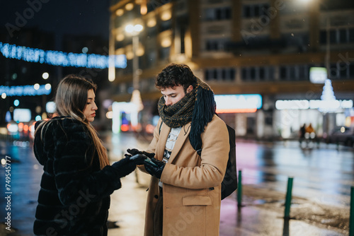 Couple sharing smart phone on city street at night, winter fashion, urban life