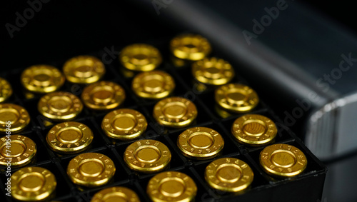 Golden ammunitions in box case with blurred short pistol magazine on black background, represents related to the concept of abstract weapons.