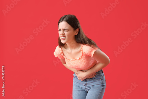 Young woman suffering from stomach ache on red background photo