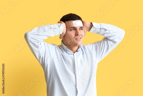 Young man with brain concussion and medical patch on yellow background