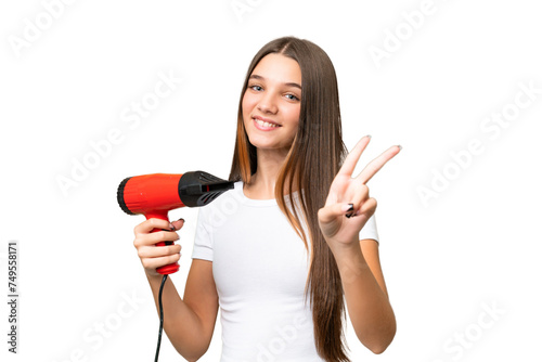 Teenager Caucasian girl holding a hairdryer over isolated background smiling and showing victory sign