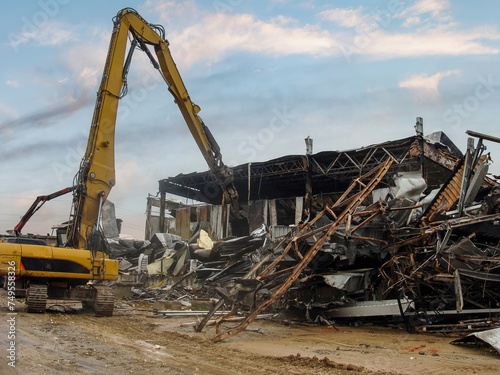 Slika na platnu Excavator dismantling the charred remains of a burnt warehouse, twisted metal st
