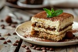 Delicious tiramisu cake on a rustic background - Close-up image of classic tiramisu dessert with layers of mascarpone and coffee-soaked ladyfingers, garnished with cocoa powder and mint leaf