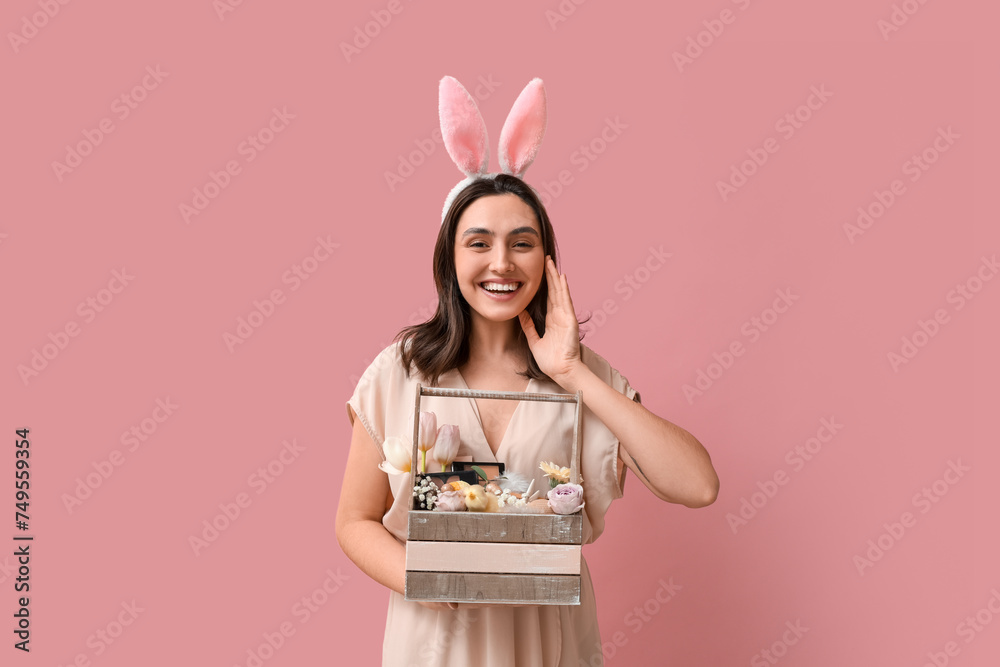 Beautiful young woman in bunny ears holding Easter basket with decorative cosmetics on pink background - obrazy, fototapety, plakaty 