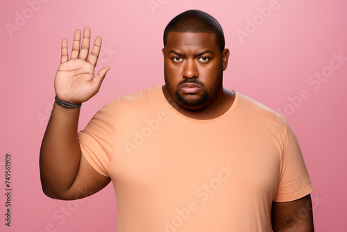 Serious displeased african american overweight man wearing basic casual orange t-shirt standing showing stop gesture with palm looking camera isolated on pastel pink background studio portrait © missty